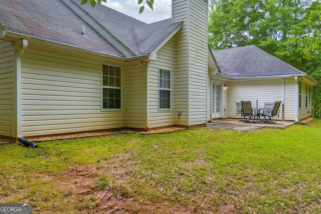 rear view of house featuring a patio, a chimney, a yard, and a shingled roof