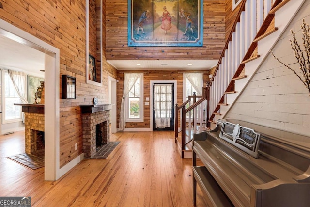 foyer featuring a fireplace, a high ceiling, wooden walls, light wood-type flooring, and stairs