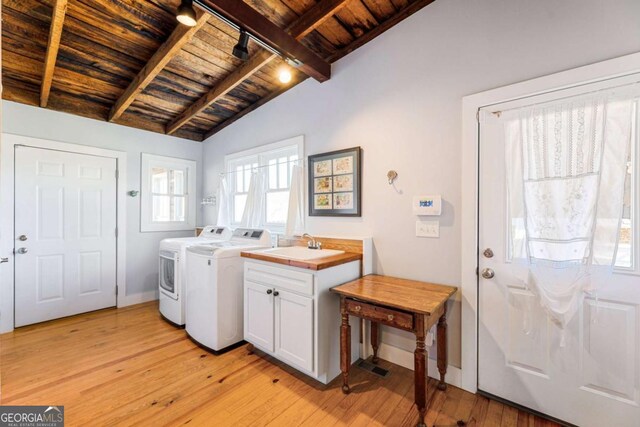 clothes washing area featuring wood ceiling, washing machine and dryer, light wood-type flooring, cabinet space, and baseboards