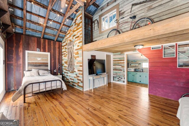 bedroom featuring wood walls, hardwood / wood-style floors, and high vaulted ceiling