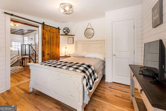 bedroom featuring light wood-type flooring, a barn door, and wood walls