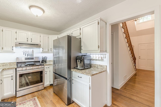 4314 Arbor Bridge Ct, Marietta, GA 30066 - kitchen featuring appliances with stainless steel finishes, under cabinet range hood, light wood-style flooring, a textured ceiling, and light stone countertops