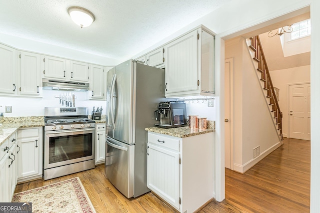 4314 Arbor Bridge Ct, Marietta, GA 30066 - kitchen featuring appliances with stainless steel finishes, under cabinet range hood, light wood-style flooring, light stone countertops, and a textured ceiling