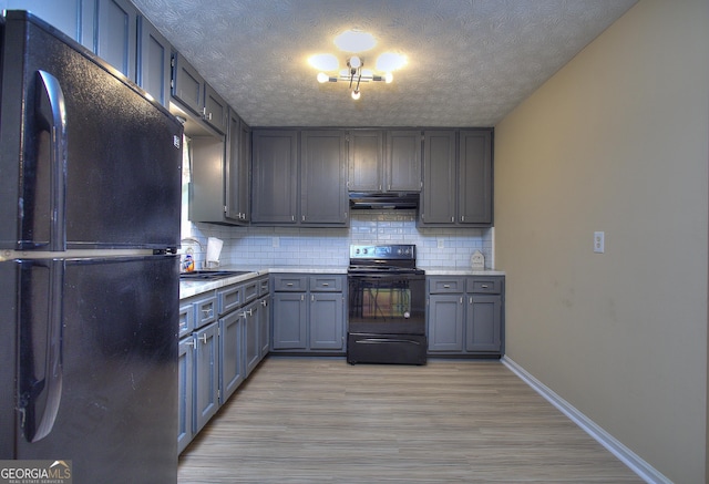 kitchen featuring black appliances, under cabinet range hood, a sink, backsplash, and a textured ceiling