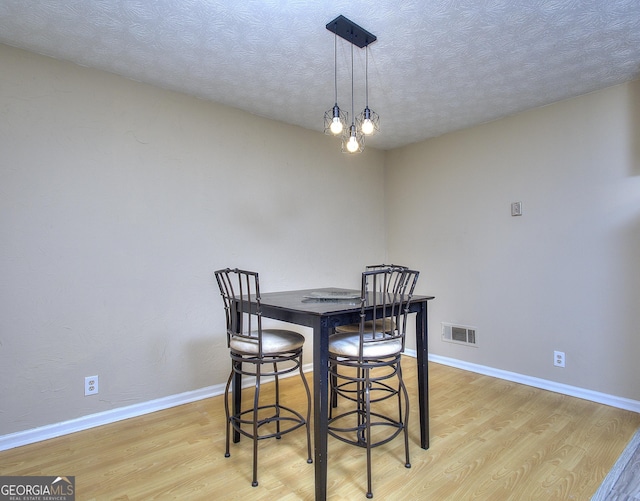 dining space featuring light wood-style flooring, baseboards, and a textured ceiling