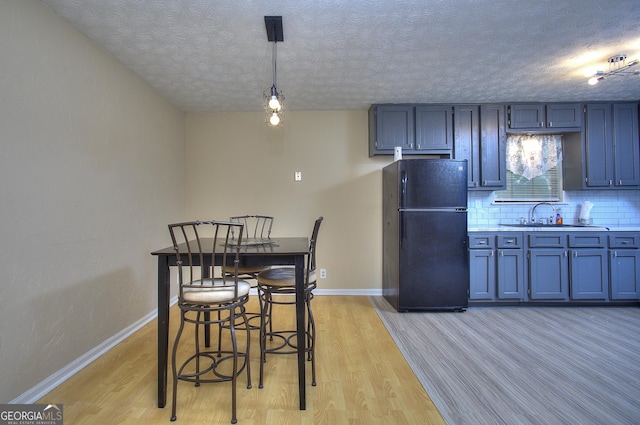 kitchen with freestanding refrigerator, a sink, a textured ceiling, light wood-style flooring, and light countertops
