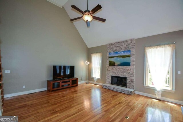 unfurnished living room with ceiling fan, healthy amount of natural light, a stone fireplace, high vaulted ceiling, and light wood-style floors