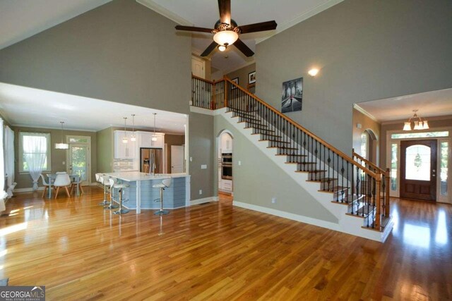 living room with stairway, light wood finished floors, a towering ceiling, baseboards, and crown molding
