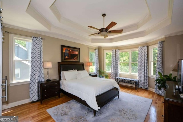 bedroom featuring ornamental molding, a raised ceiling, wood finished floors, a ceiling fan, and baseboards