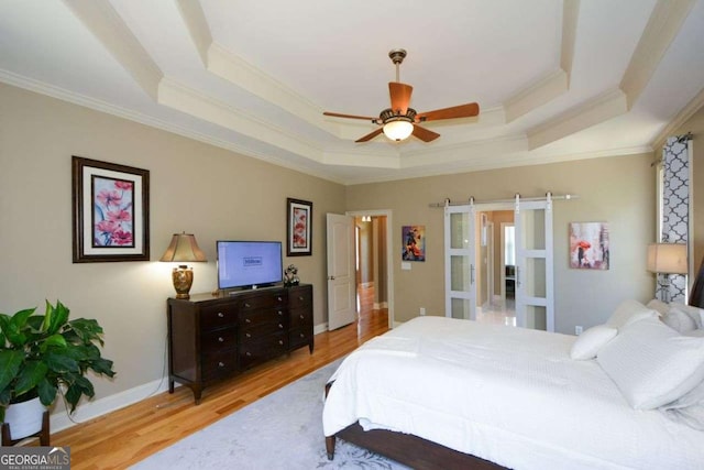 bedroom featuring a tray ceiling, ornamental molding, wood finished floors, a ceiling fan, and baseboards