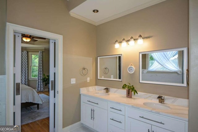 ensuite bathroom with double vanity, wood finished floors, crown molding, baseboards, and a ceiling fan