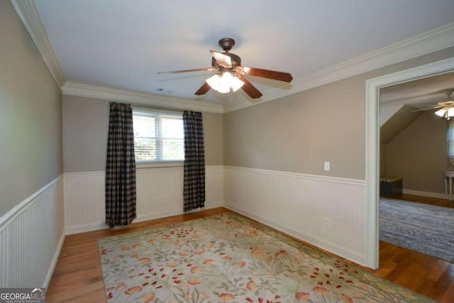 spare room with ceiling fan, wood finished floors, wainscoting, and ornamental molding