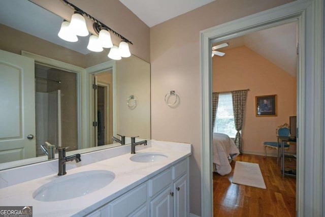 ensuite bathroom featuring wood finished floors, double vanity, vaulted ceiling, and baseboards