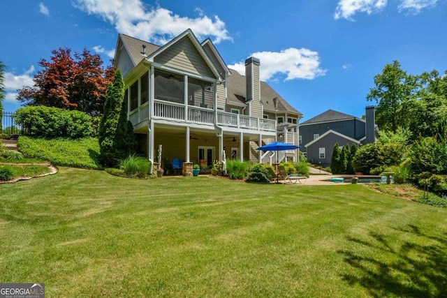 back of property with ceiling fan, a sunroom, a yard, a chimney, and a patio