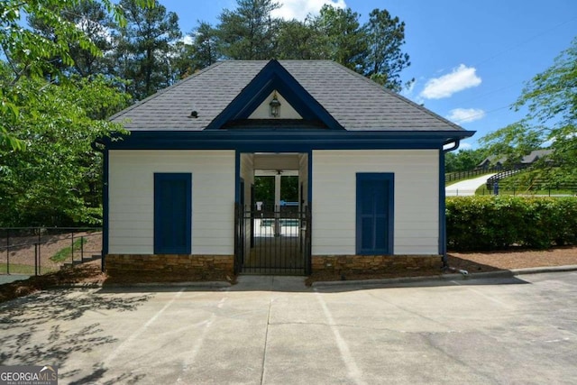 rear view of property featuring fence, stone siding, a shingled roof, and a porch