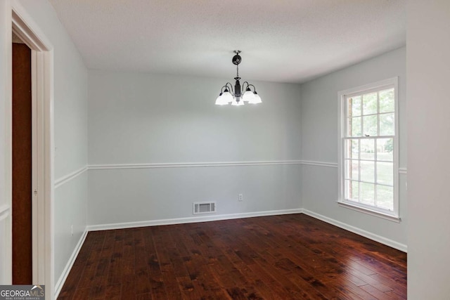 empty room with dark wood-type flooring, a chandelier, and baseboards