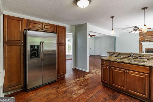 kitchen with stainless steel refrigerator with ice dispenser, a ceiling fan, a sink, open floor plan, and light stone counters