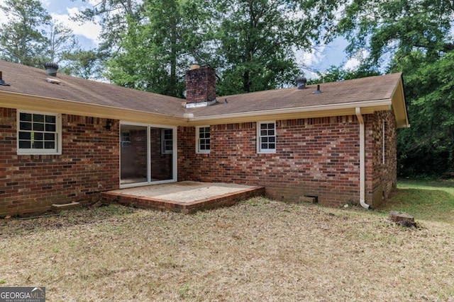 back of property featuring a chimney, a patio, brick siding, and roof with shingles
