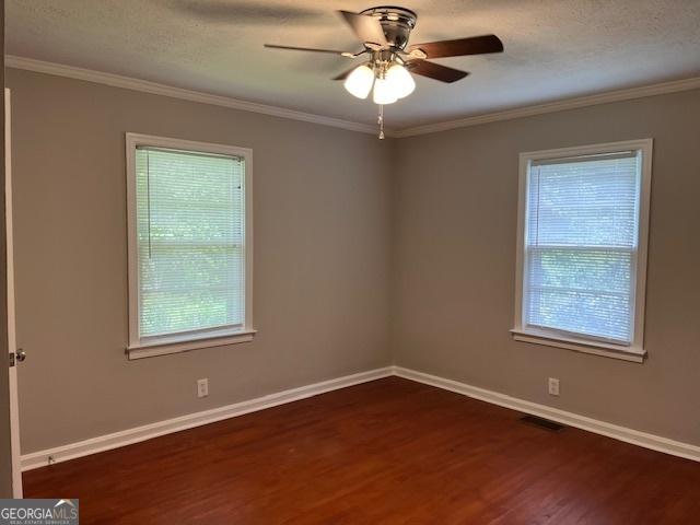 empty room with plenty of natural light, dark wood-style floors, baseboards, ceiling fan, and ornamental molding