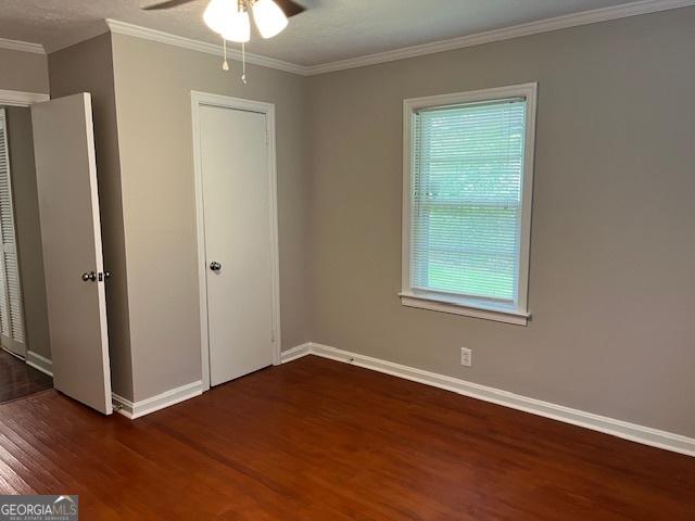 unfurnished bedroom featuring wood finished floors, baseboards, crown molding, and a ceiling fan