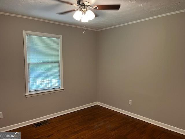 spare room with dark wood-type flooring, ceiling fan, ornamental molding, baseboards, and a textured ceiling