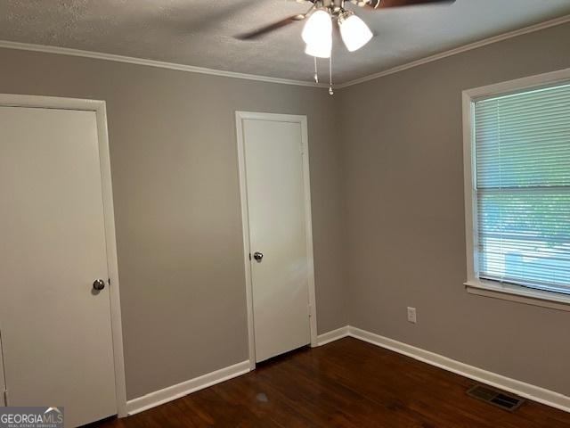 unfurnished bedroom with dark wood finished floors, ornamental molding, baseboards, and ceiling fan