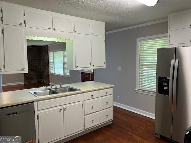 kitchen featuring appliances with stainless steel finishes, a sink, dark wood-type flooring, white cabinetry, and baseboards
