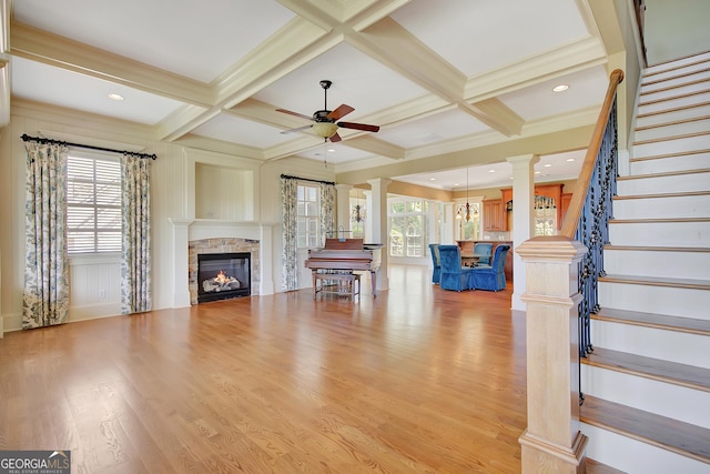 living area with a ceiling fan, ornate columns, light wood finished floors, stairs, and a stone fireplace