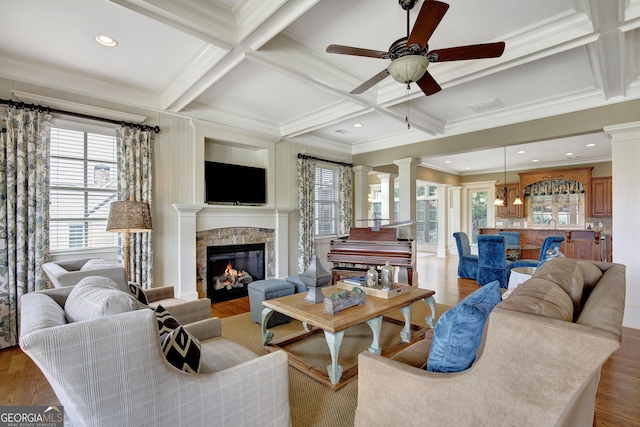 living area with decorative columns, crown molding, a ceiling fan, coffered ceiling, and light wood-style floors
