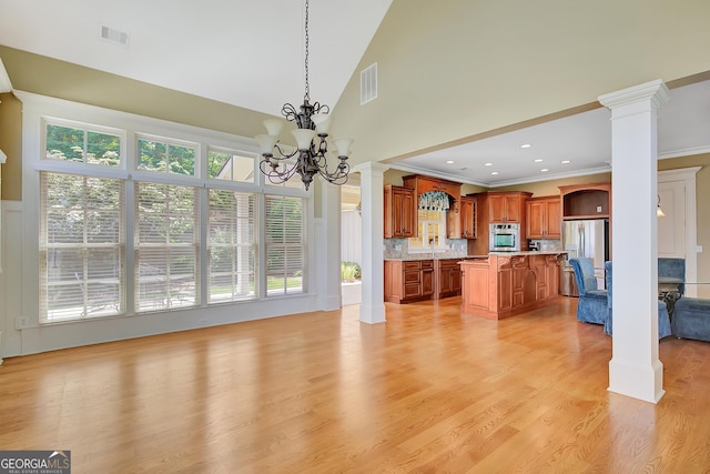unfurnished dining area with ornate columns, ornamental molding, a chandelier, light wood-style floors, and high vaulted ceiling