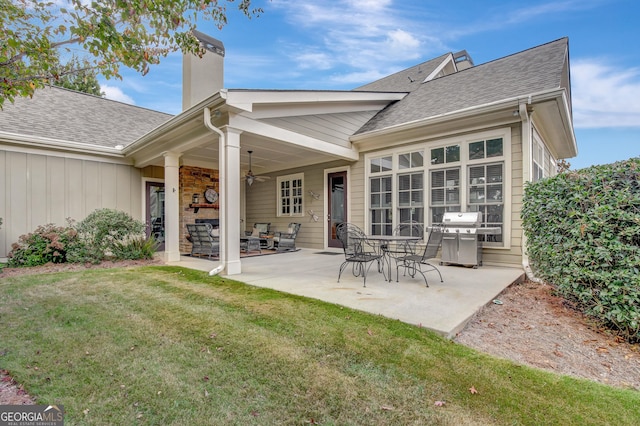 back of property featuring a chimney, a yard, a ceiling fan, a shingled roof, and a patio