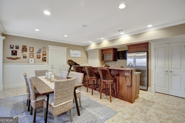 dining space with crown molding, recessed lighting, a wainscoted wall, and bar