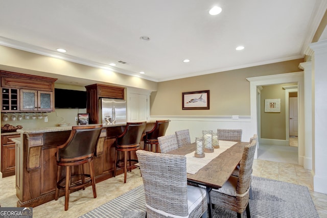 dining room with wet bar, recessed lighting, ornamental molding, and a wainscoted wall