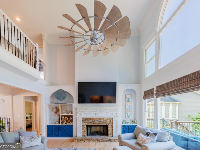 living room with a high ceiling, ornamental molding, built in shelves, wood finished floors, and a stone fireplace