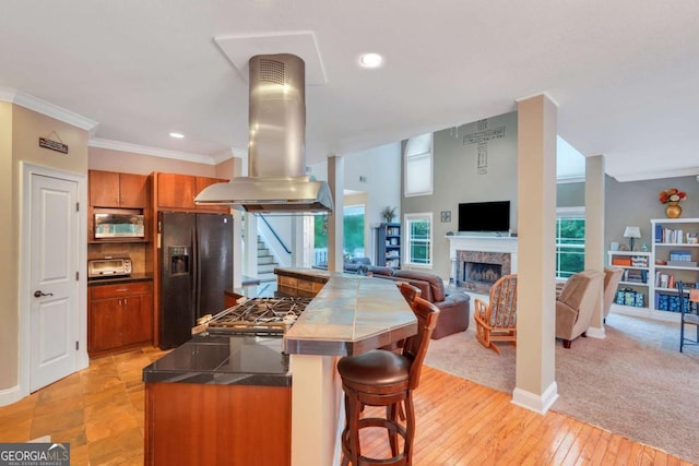 kitchen featuring black fridge, island exhaust hood, open floor plan, brown cabinets, and dark countertops