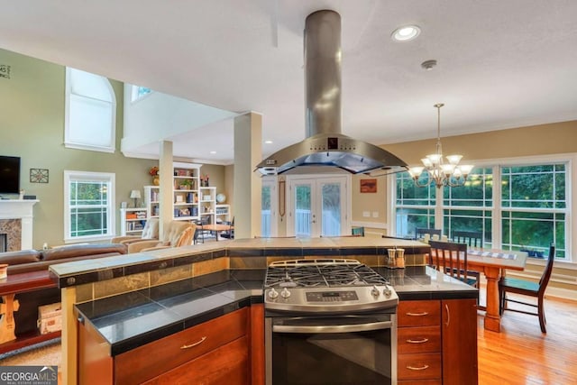 kitchen with stainless steel range with gas stovetop, open floor plan, island exhaust hood, brown cabinetry, and recessed lighting
