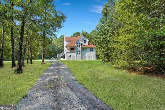view of front facade with driveway, a chimney, stairway, and a front yard