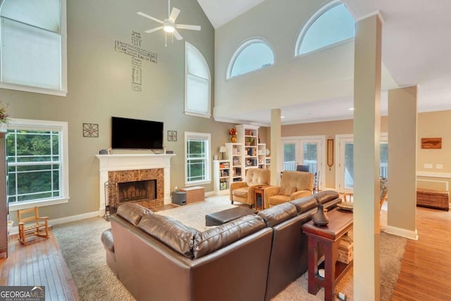 living room featuring wood finished floors, ceiling fan, high vaulted ceiling, baseboards, and a fireplace