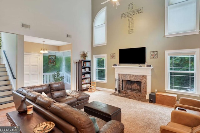 carpeted living area with a high ceiling, a high end fireplace, stairs, baseboards, and a ceiling fan