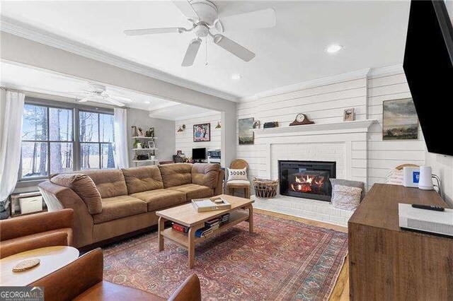 living room featuring a ceiling fan, crown molding, a fireplace, wood finished floors, and recessed lighting