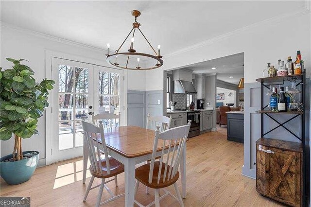 dining area featuring healthy amount of natural light, a chandelier, french doors, light wood-style floors, and ornamental molding