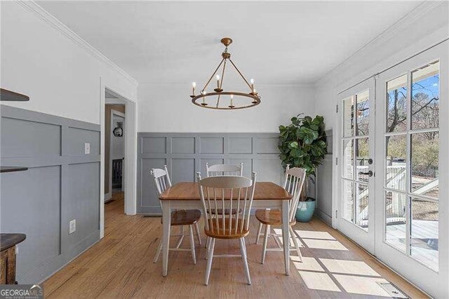 dining space featuring a decorative wall, light wood-style flooring, crown molding, a chandelier, and french doors