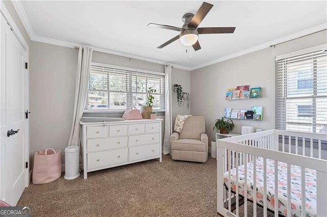 bedroom with a crib, crown molding, carpet flooring, and a ceiling fan