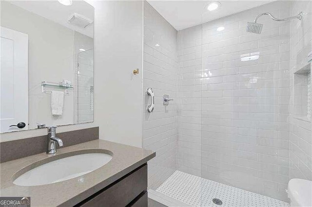 bathroom with tiled shower, vanity, and recessed lighting