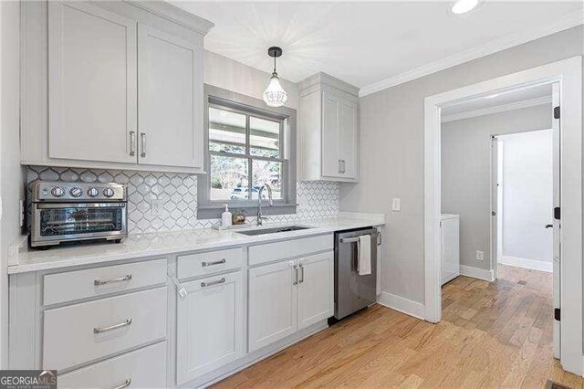 kitchen with stainless steel dishwasher, a sink, ornamental molding, decorative backsplash, and light wood-style floors