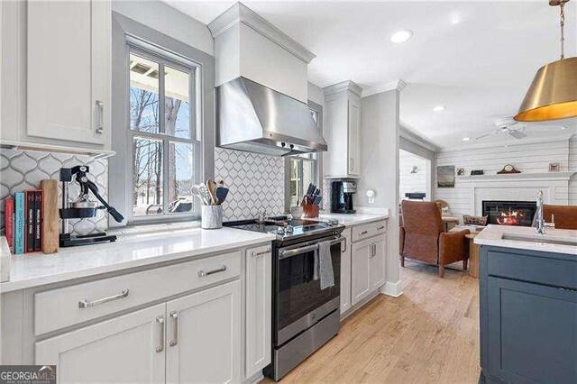 kitchen with electric stove, wall chimney range hood, a sink, open floor plan, and light wood finished floors