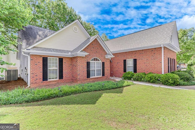 view of front of property featuring a shingled roof, brick siding, central AC unit, and a front yard