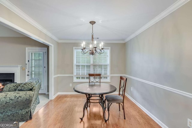 dining room featuring light wood-style flooring, a warm lit fireplace, a chandelier, crown molding, and baseboards