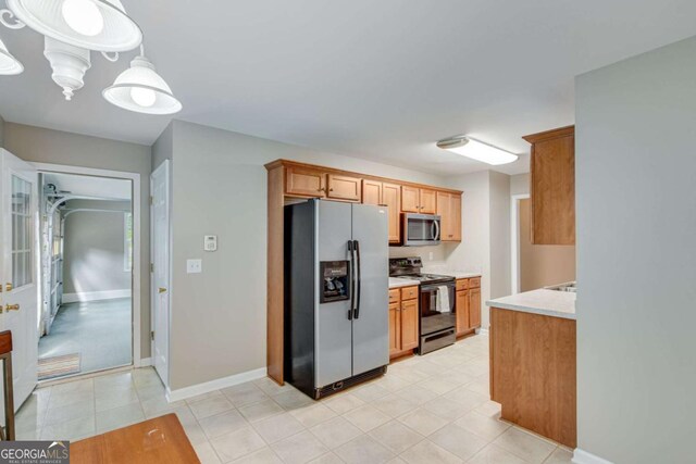 kitchen featuring appliances with stainless steel finishes, light countertops, light tile patterned flooring, baseboards, and brown cabinets