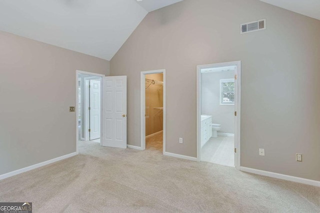 unfurnished bedroom with a walk in closet, a closet, high vaulted ceiling, carpet floors, and ensuite bathroom